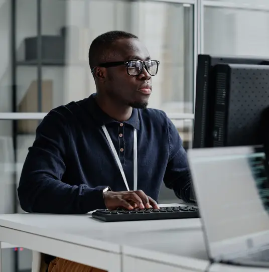 Homem de óculos digitando em um teclado em frente ao monitor